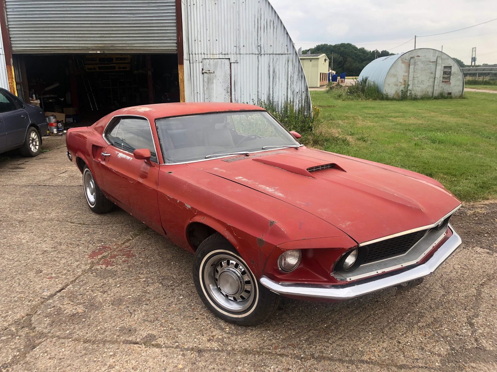 Red 1969 Mustang Mach 1 with a bonnet scoop, parked outdoors, seen from the front left