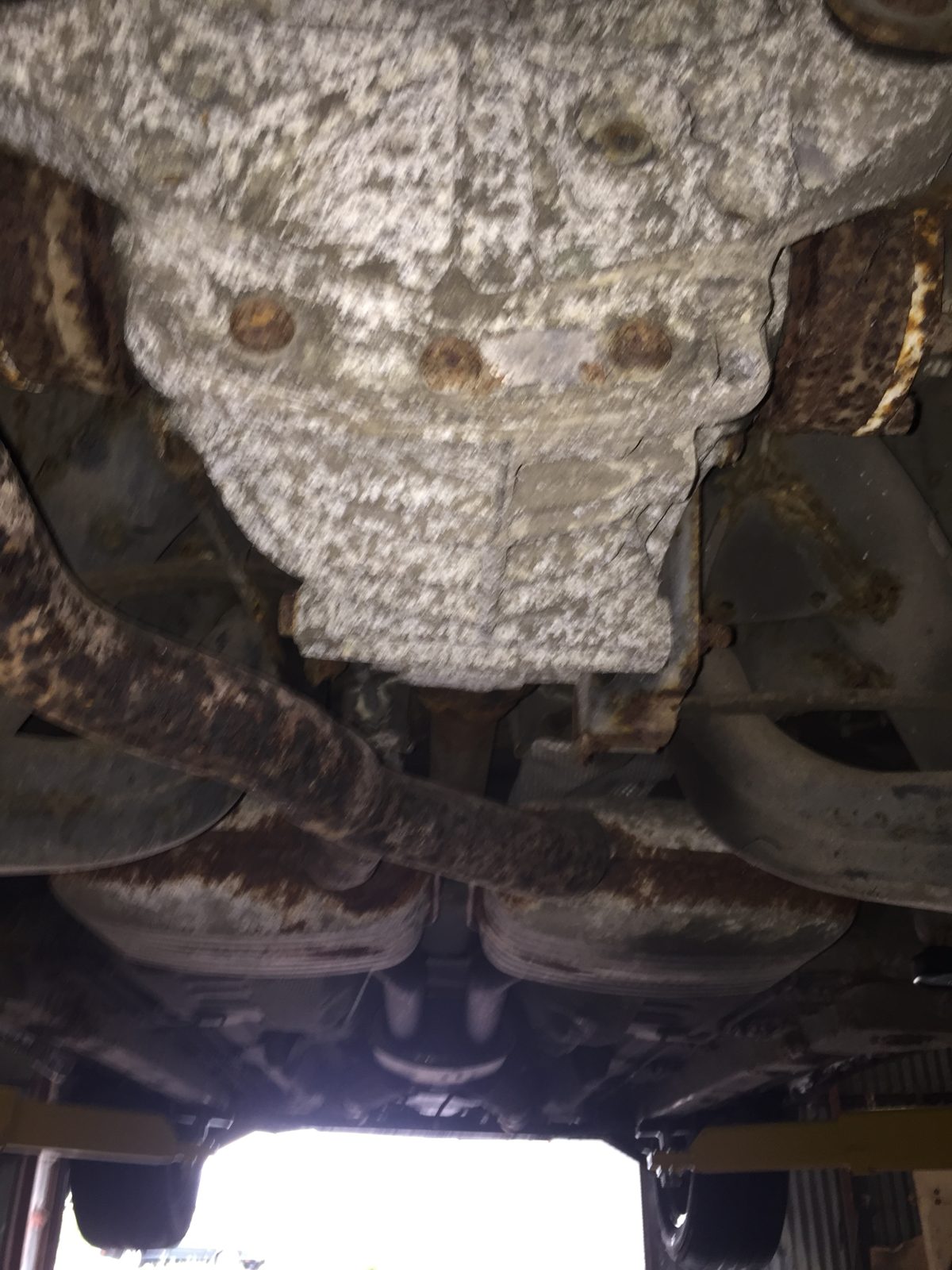 Underside of the car, with a stone-chipped fuel tank above a rusty exhaust