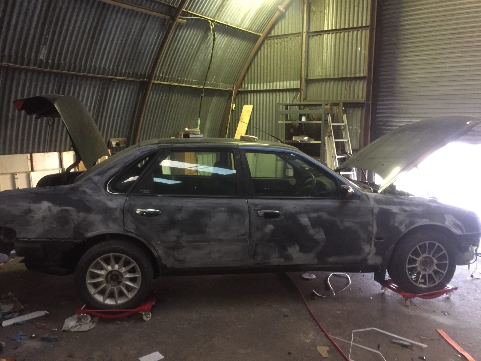 The shell in primer in the workshop, bonnet and boot open, standing on dollies
